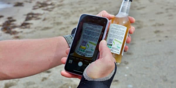 Photo of a smartphone scanning a qr code from a bottle with a beach in the background