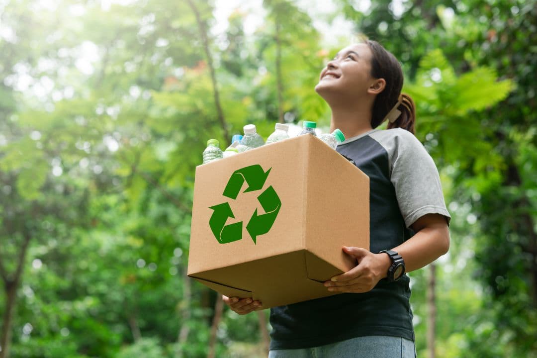 Photo of a lady holding a cardboard box with a recycling symbol on the side