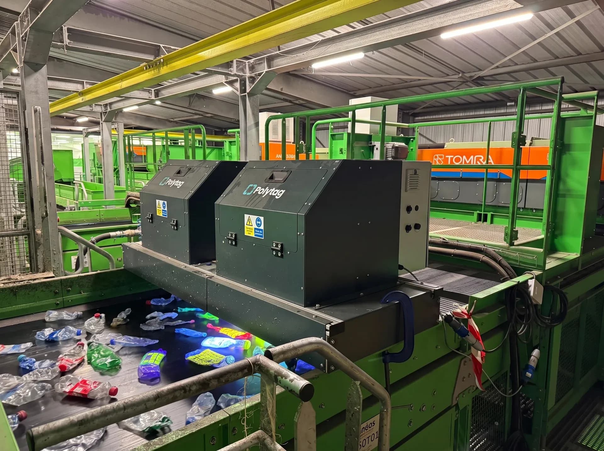 Two Polytag UV detection units over a recycling-centre conveyor, tagged bottles glowing beneath them