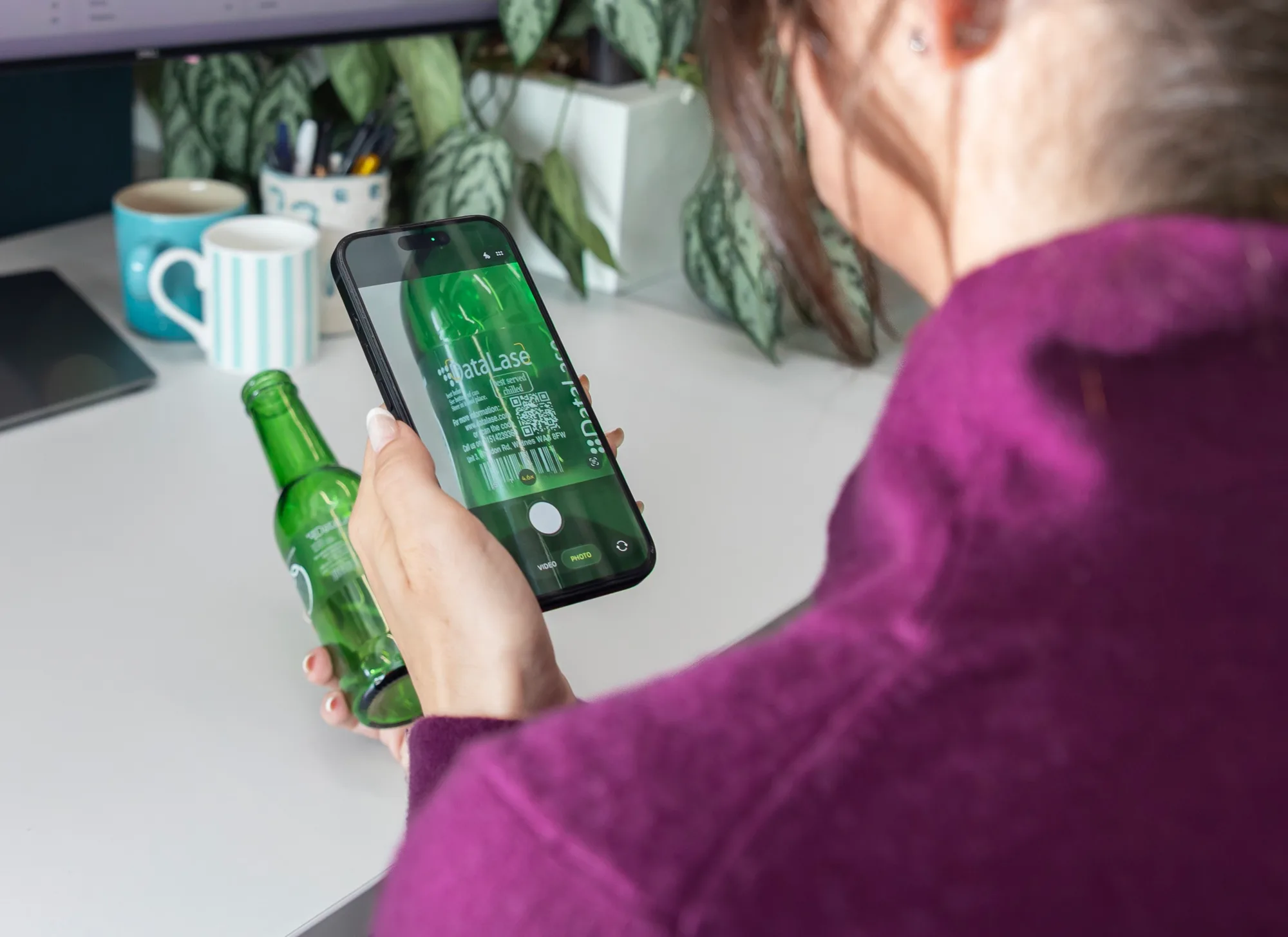 Una persona que escanea con su móvil el código marcado con láser en una botella de cristal verde