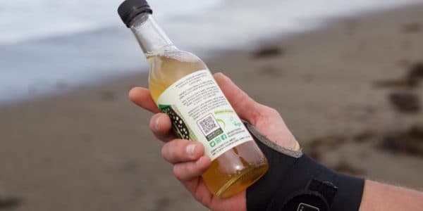 Photo of a person looking at a label on a glass bottle with a beach in the background