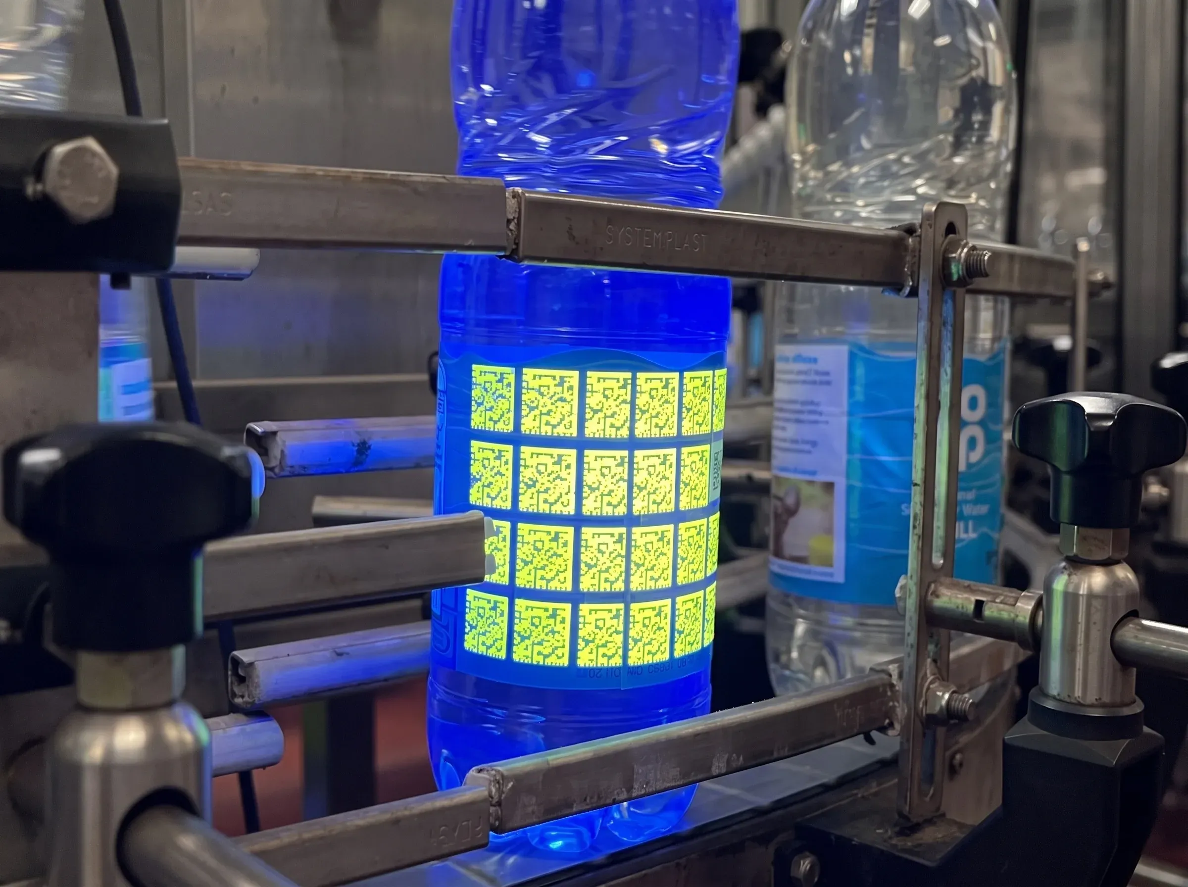 A Co-op water bottle on a conveyor under UV light, its Invisible UV Tags glowing across the label