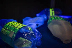 Photo de bouteilles en plastique portant des étiquettes UV invisibles révélées sous lumière UV.